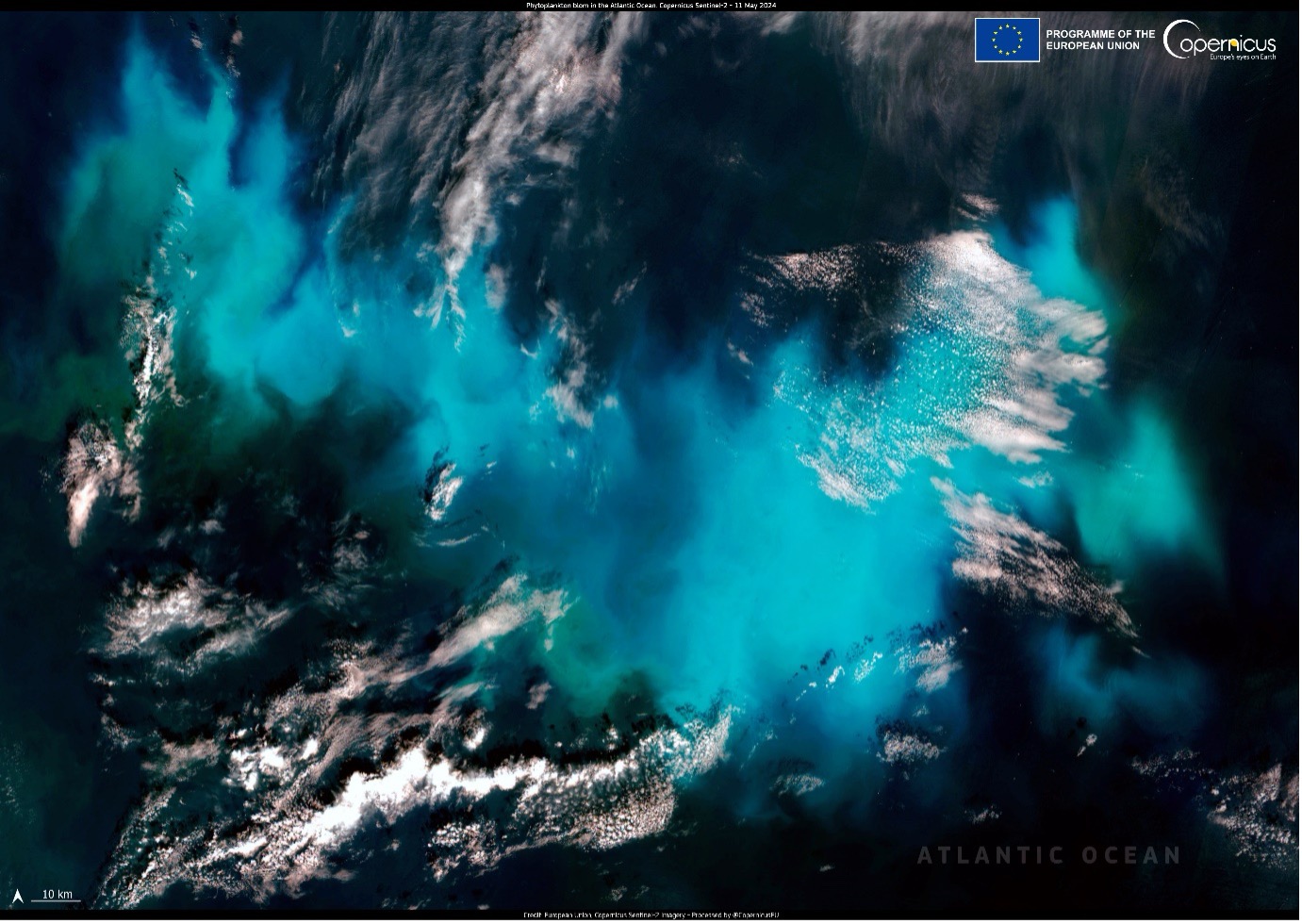 The image, acquired by the Copernicus Sentinel-2 satellite on 11 May 2024, shows a stunning phytoplankton bloom in the Atlantic Ocean, west of the French coast. The natural-colour visualisation features vibrant swirls of turquoise and deep blue, illustrating the dense concentration of phytoplankton. White clouds scattered across the image provide a striking contrast against the vivid blue-green bloom. The bottom left corner includes a scale bar indicating 10 km, and the top right corner displays logos for the European Union and Copernicus.